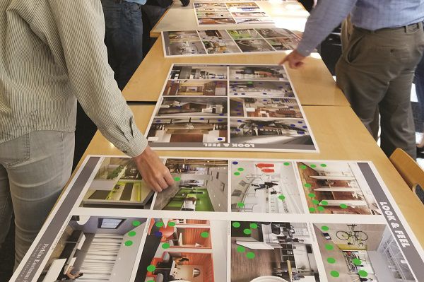 Three design concept posters laying on table tops with two different hands pointing at the images on the poster